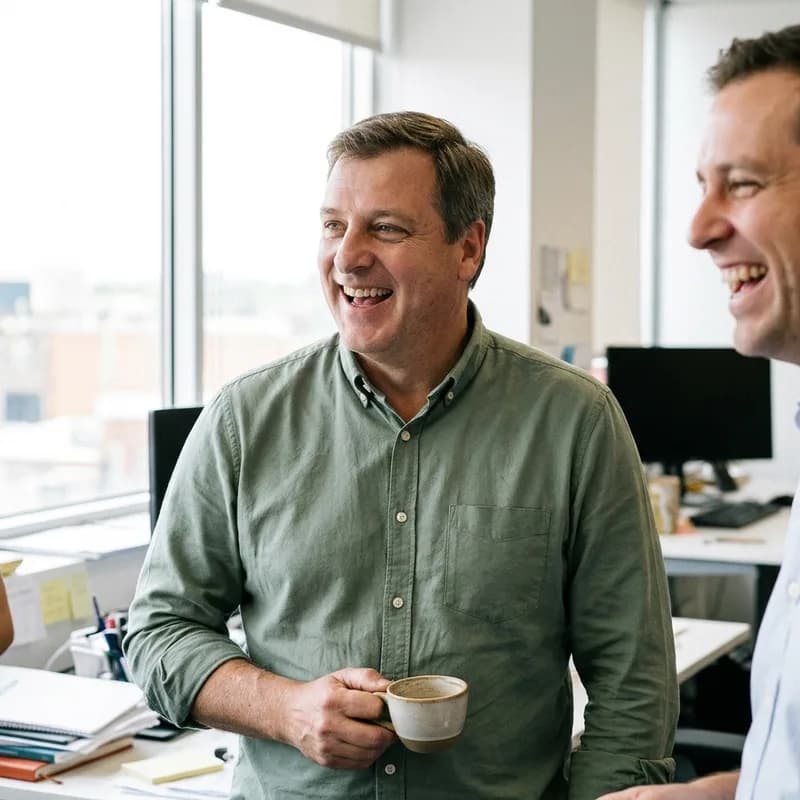 A man in a green shirt laughing with a coworker in a bright office